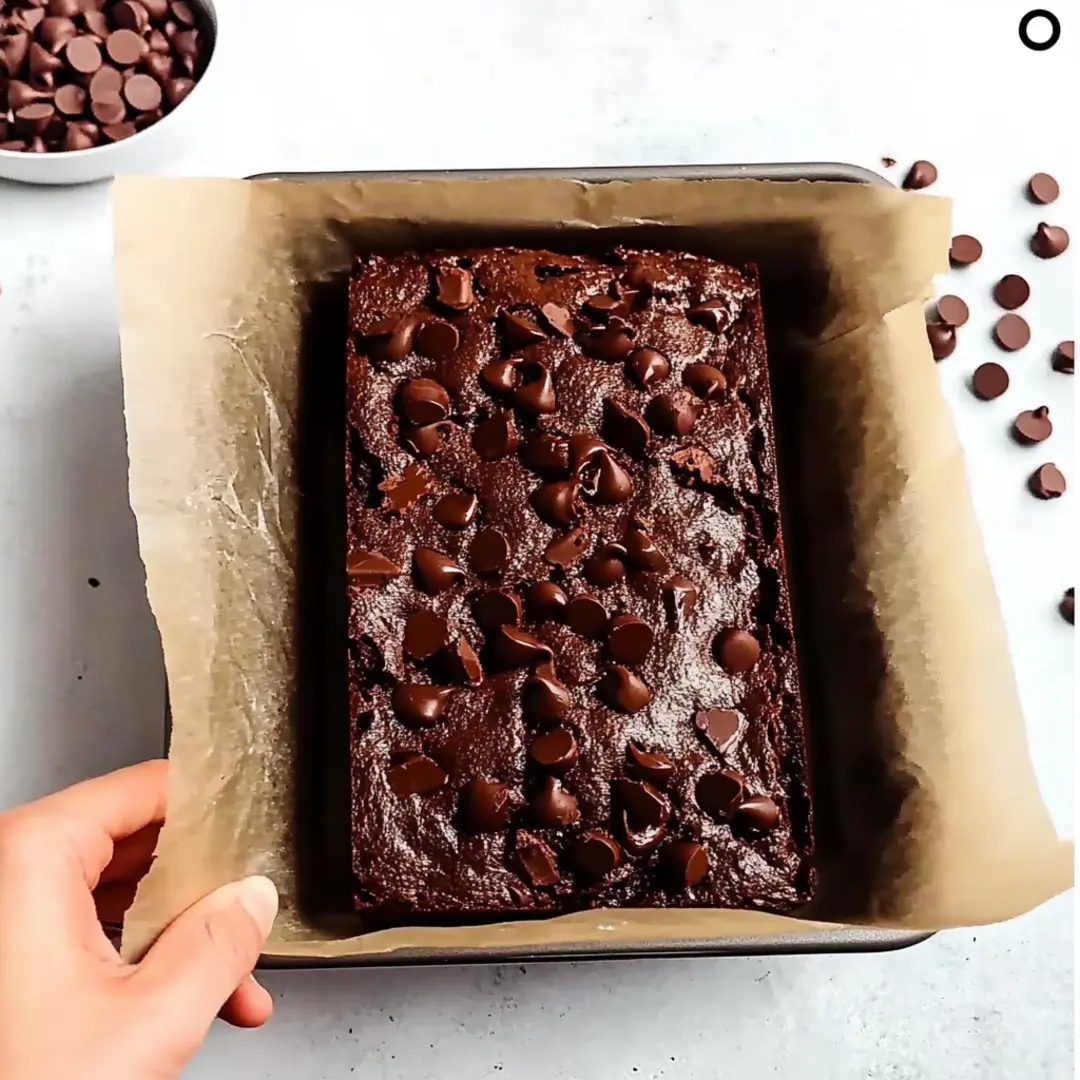 Freshly baked chocolate bread in a parchment-lined pan, topped with melted chocolate chips.