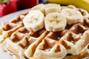 Golden waffle topped with banana slices, sprinkled with powdered sugar.