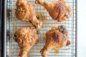 Four golden-brown fried chicken drumsticks cooling on a wire rack.