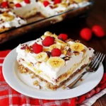 Top view of a no-bake banana split cake in a glass dish, topped with bananas, cherries, and graham cracker crumbs.