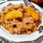 A bowl of peach crumble with vibrant peaches and a crunchy topping, served on a vintage-style plate.