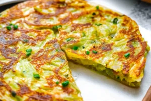 Close-up of a crispy cabbage pancake garnished with green onions, cut into slices.