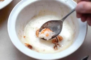 Close-up of a spoon scooping creamy crab custard from a white ramekin during the preparation of crab brulee.