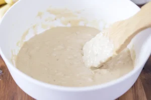 Banana waffle batter being stirred in a white mixing bowl.