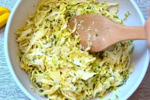 Shredded cabbage mixed with seasonings in a white bowl, stirred with a wooden spoon.