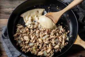 Cooking chicken and onions for a cheesesteak in a skillet with melted cheese.