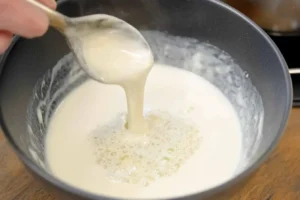 Rich and creamy Parmesan sauce being stirred in a pan with a spoon.