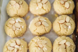 Freshly baked almond cookies topped with sliced almonds on a baking tray.