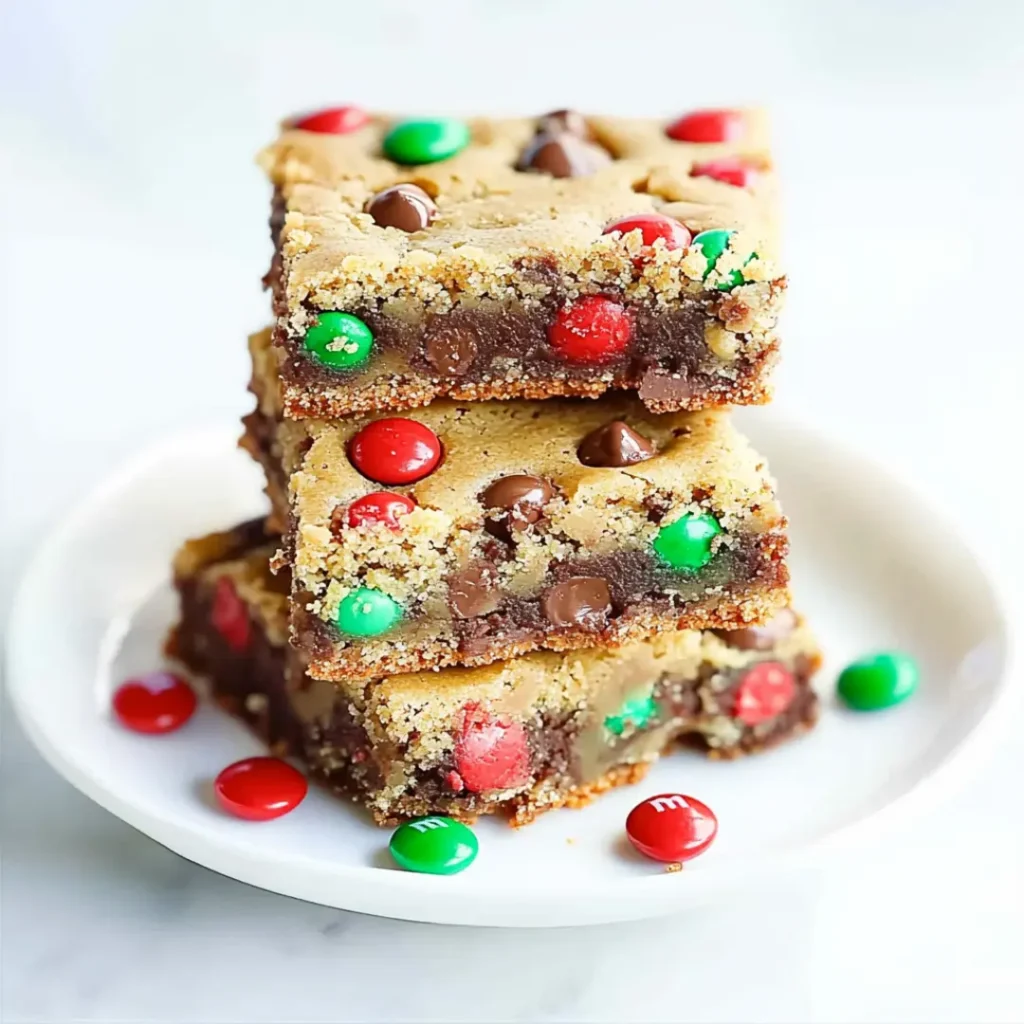 Stack of chewy M&M cookie bars with chocolate chips, featuring red and green M&M’s on a white plate.