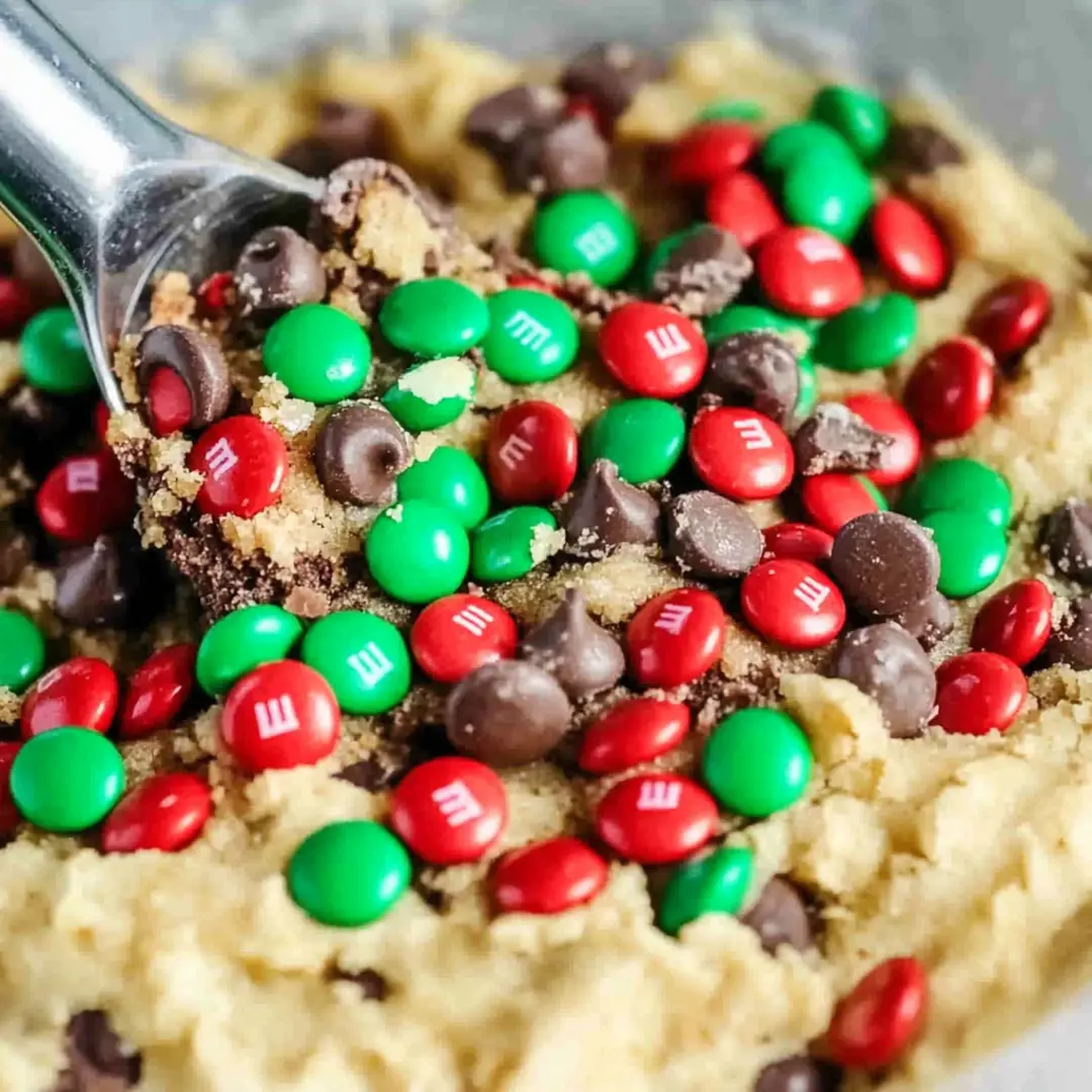 Mixing M&M’s and Chocolate Chips into Cookie Dough Festive red and green M&M’s and chocolate chips being mixed into cookie dough.