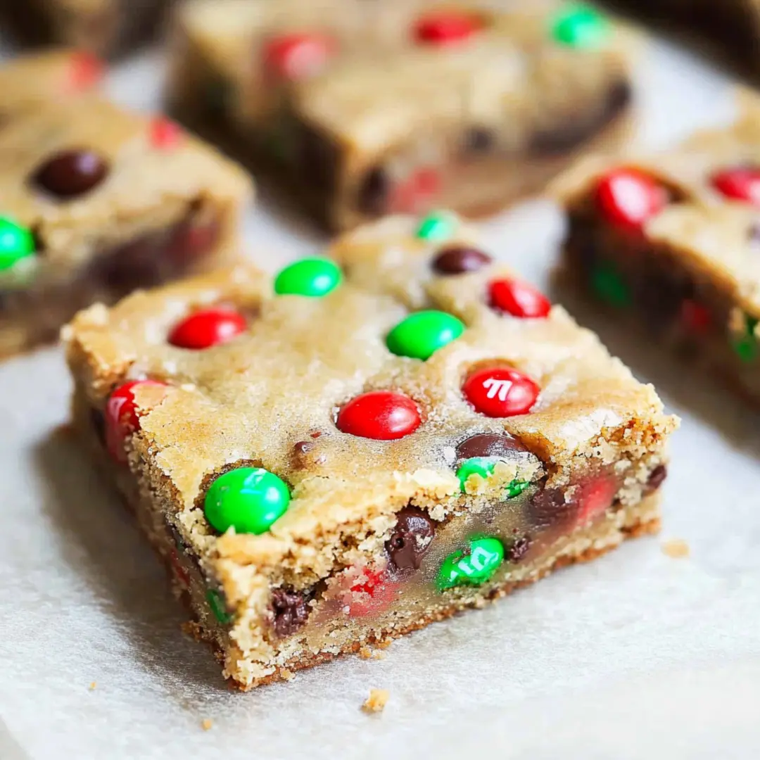 Chewy M&M Cookie Bars with Chocolate Chips Soft and chewy M&M cookie bars with red and green M&M’s, cut into squares and served on parchment paper.